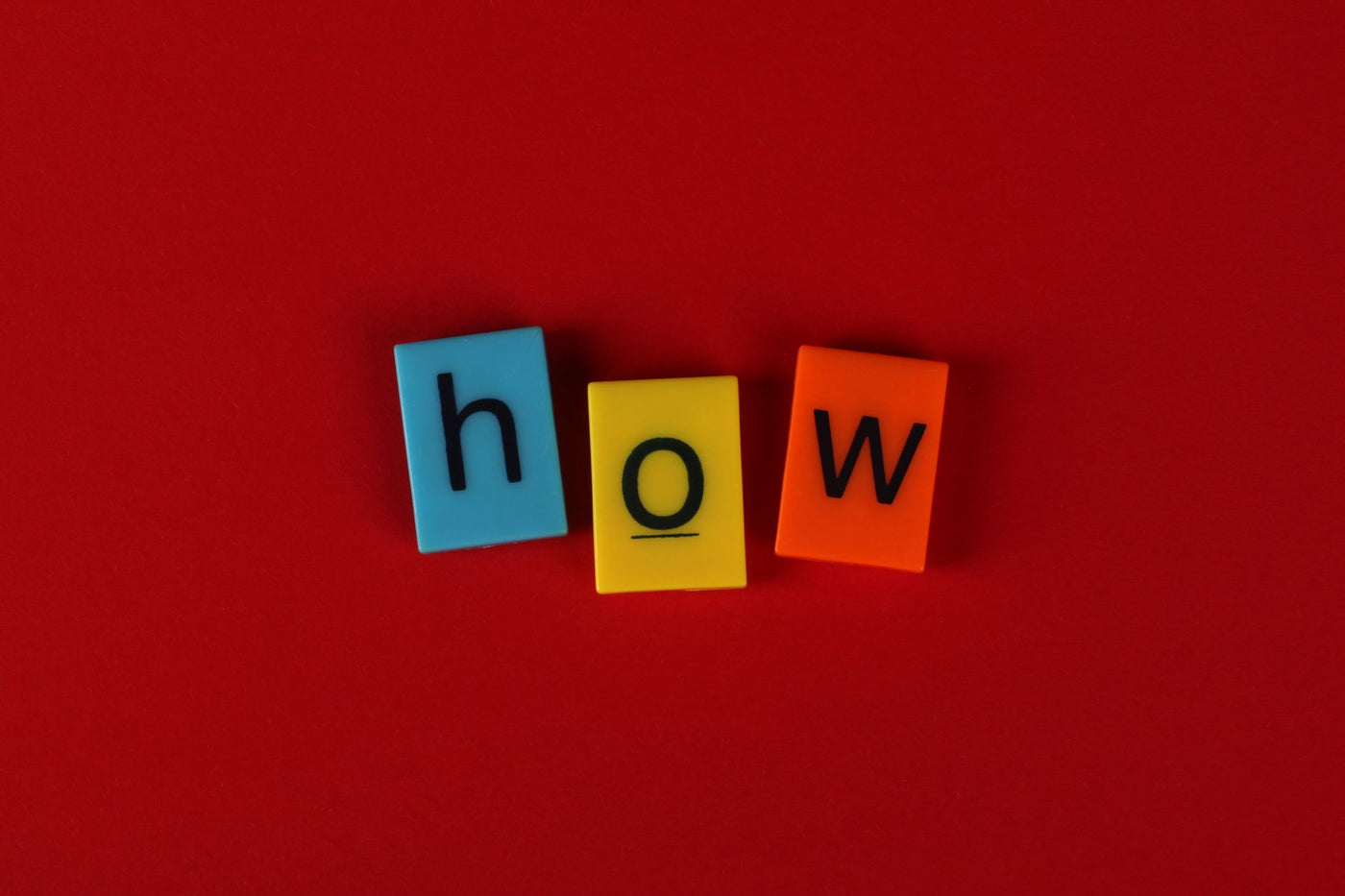 Colorful letter tiles spelling 'How' on a vibrant red background, ideal for educational content.