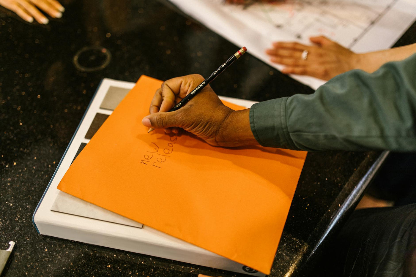 Close-up of a hand writing on an orange envelope using a pencil on a dark surface.