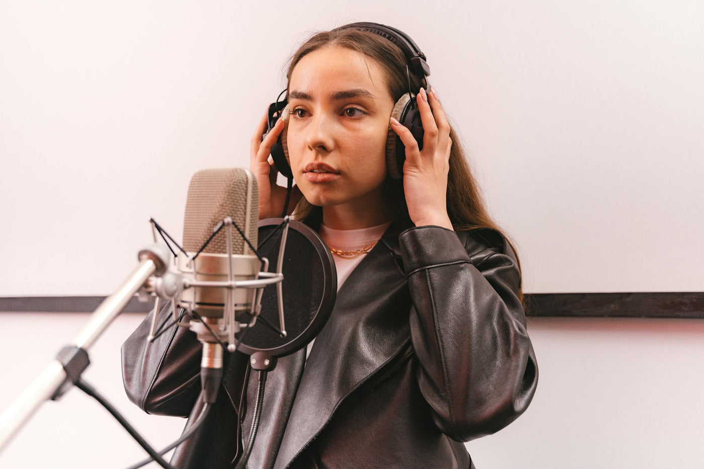 Woman in a leather jacket recording vocals in a professional studio.
