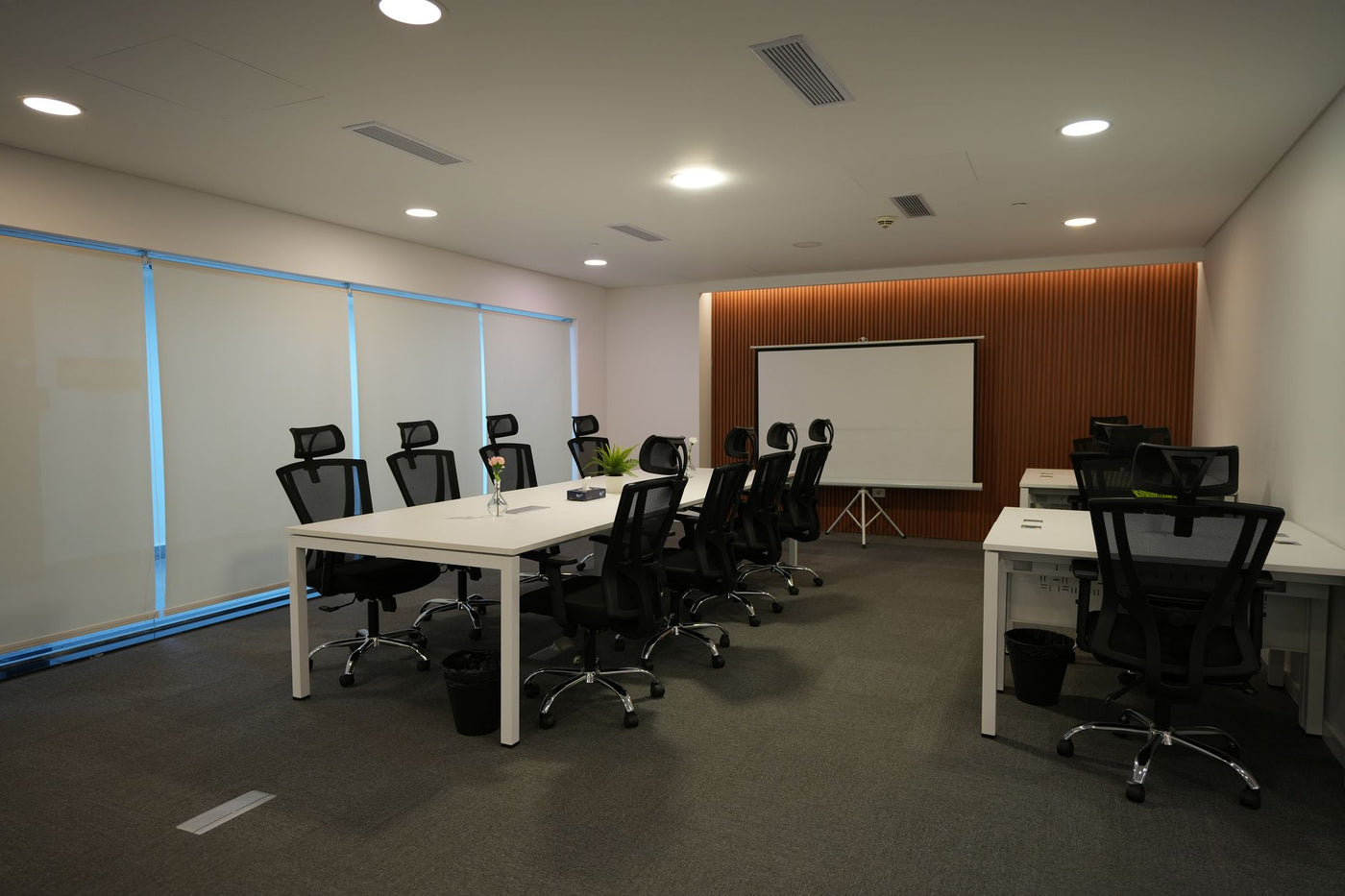 Spacious and well-lit conference room featuring ergonomic chairs, large tables, and a projector screen.