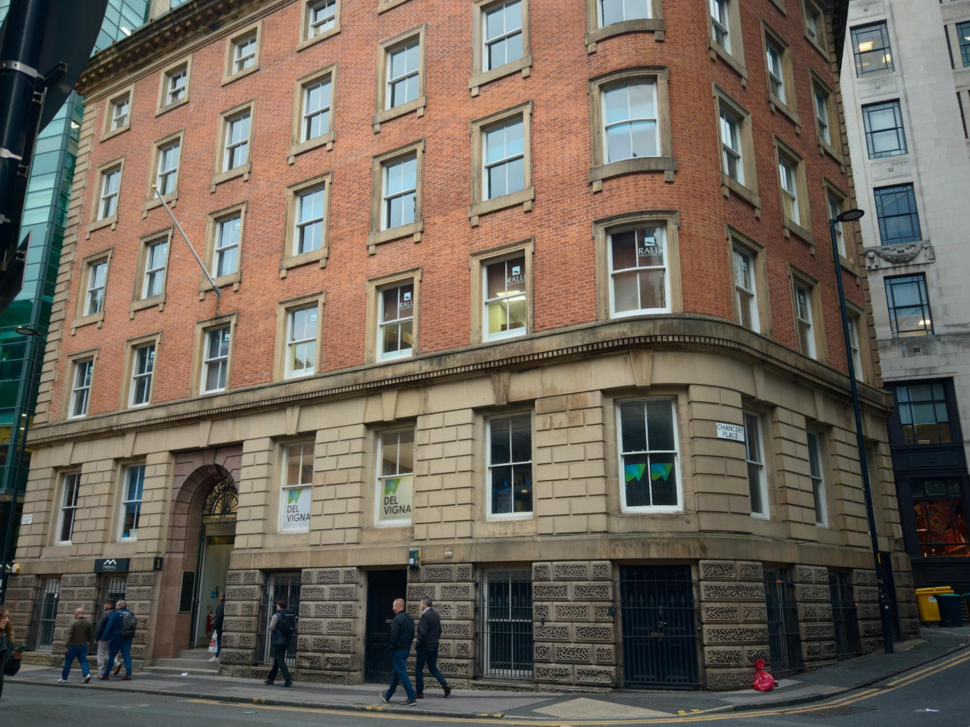 Red brick building on a street corner with pedestrians during the day.