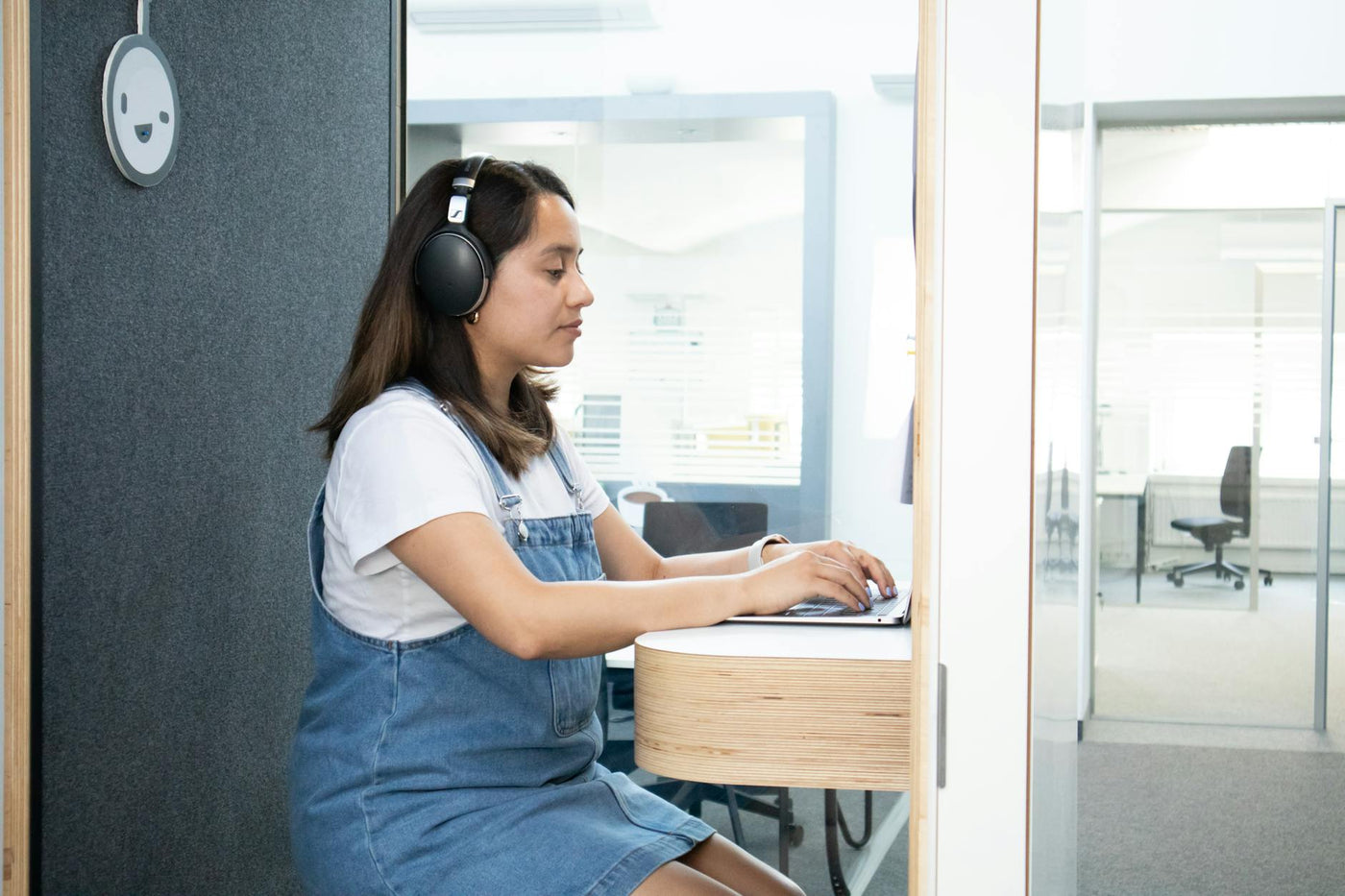 Woman using a laptop with headphones in a modern office booth, focused on tasks.