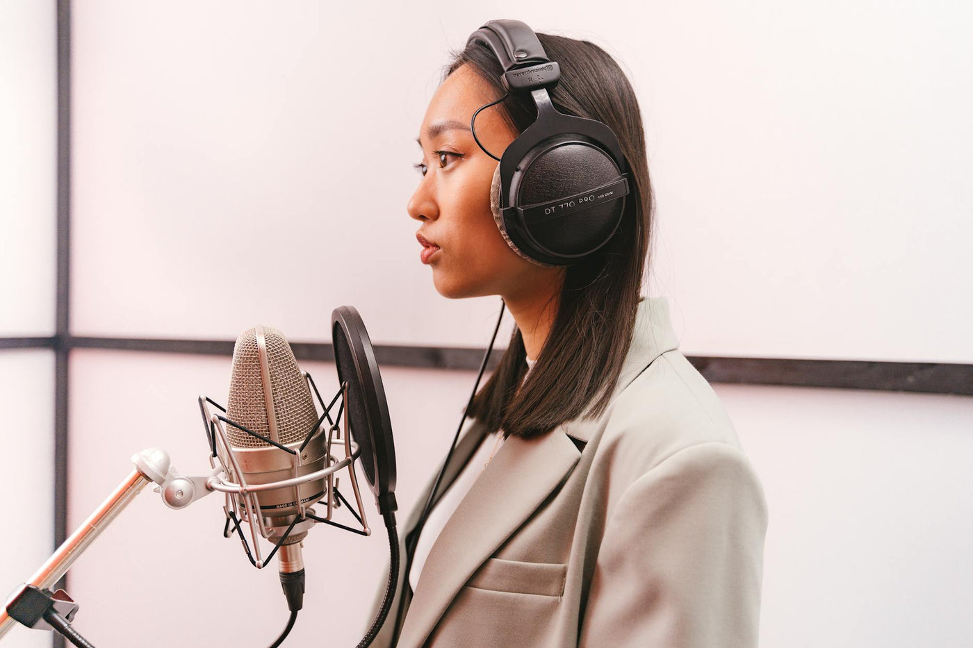 A woman in headphones singing into a condenser microphone in a music studio.